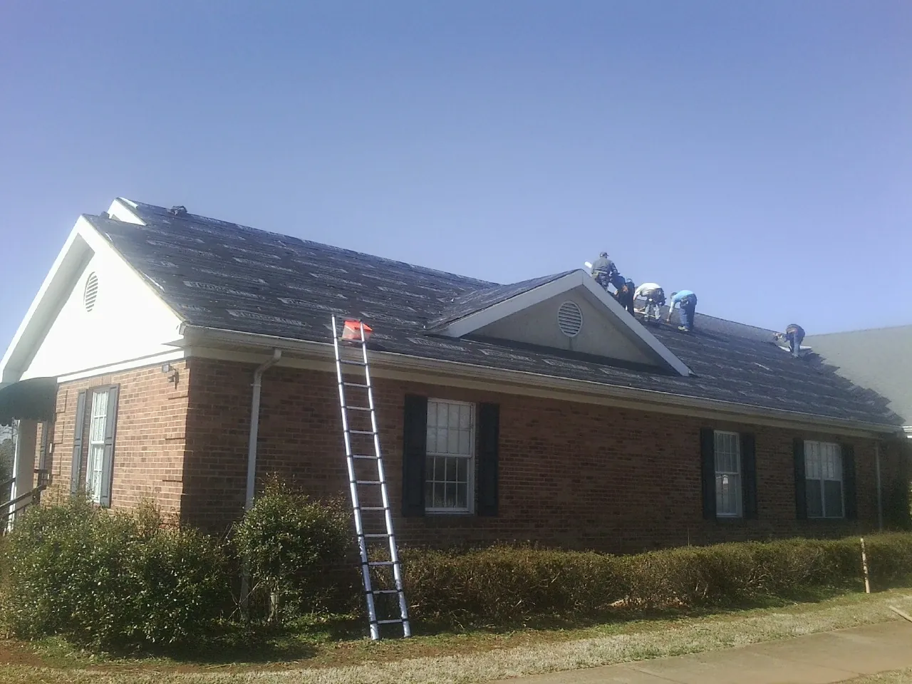 Crew tearing shingles off a brick ranch roof with a ladder set — Metal Roof Repair work by our crew in Lake Bluff