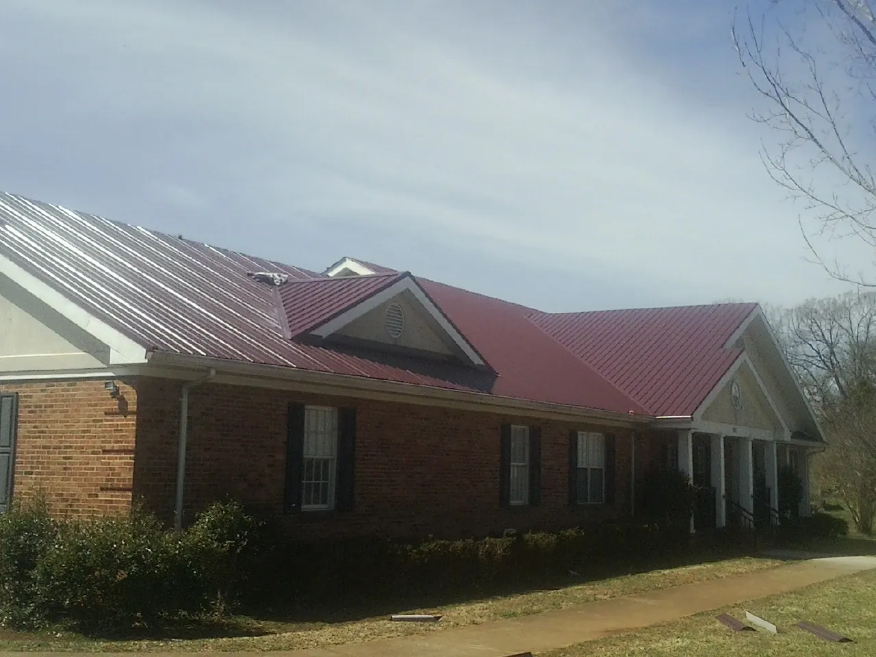 Red metal roof with gabled entries on a long brick building, from a Hail Damage Roof Repair job in Lake Bluff