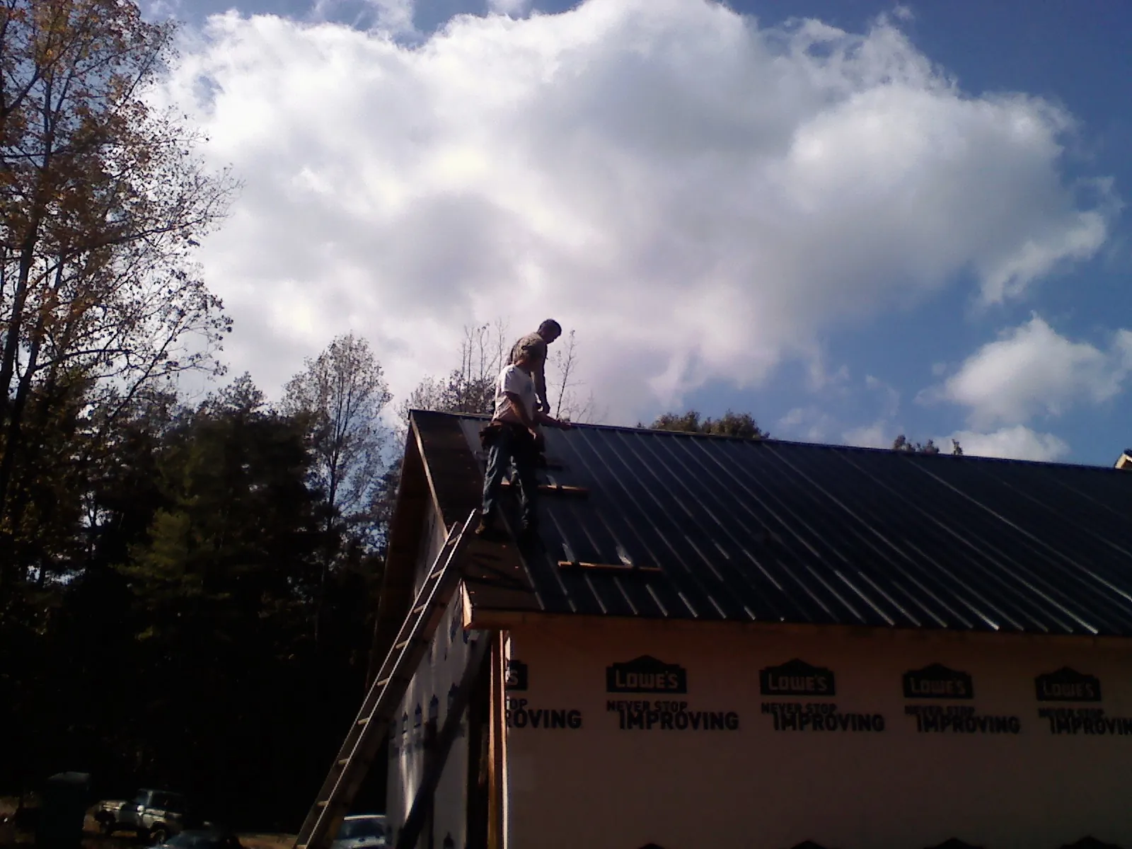 Roofer fastening dark metal panels high against a cloudy sky, from a Roof Inspection job in Lake Bluff