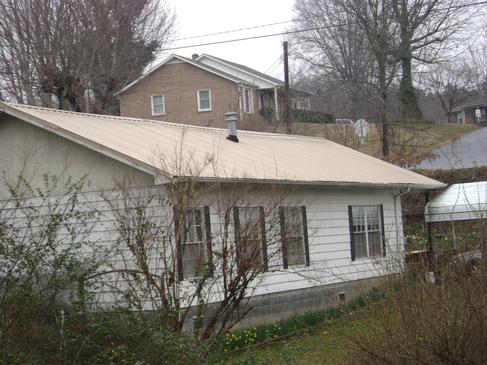 Tan metal roof on a white sided house set into a hillside — Commercial Roofing by Roofing Brothers in Lake Bluff